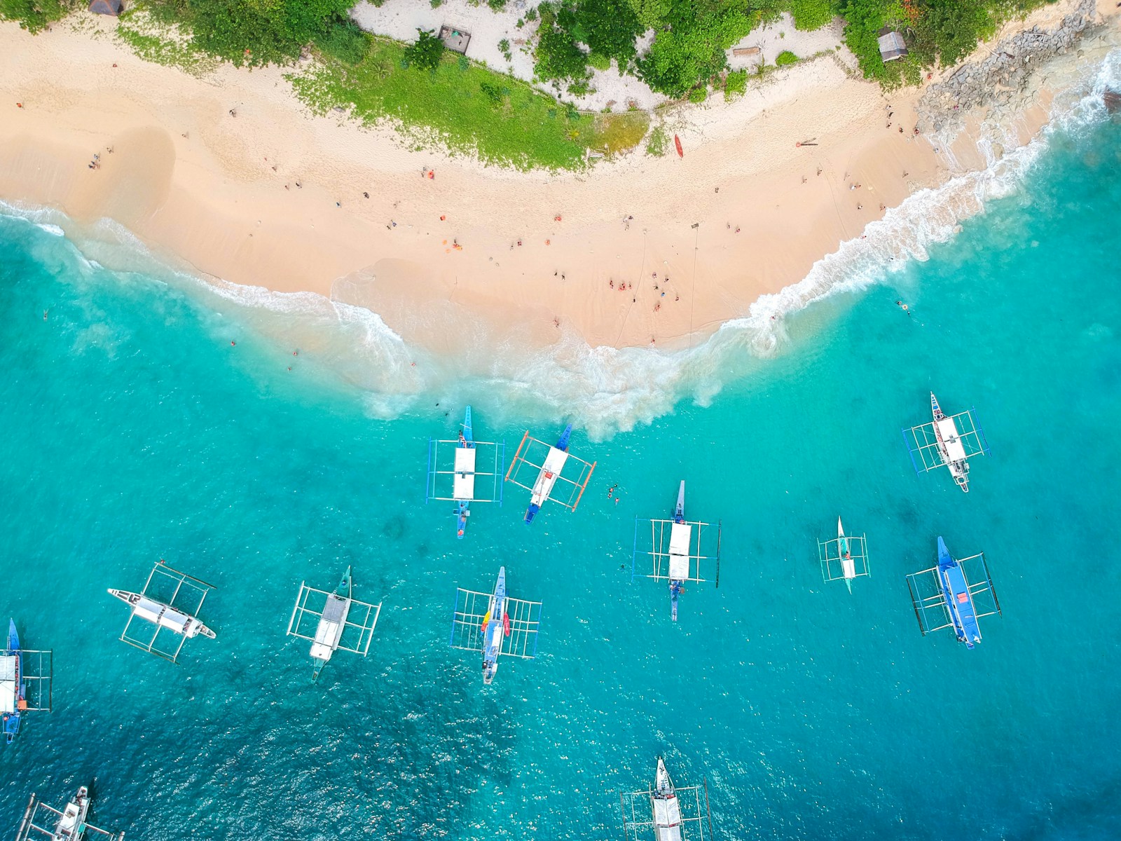 An aerial view of Filipino bangka outrigger boats anchored off a white-sand beach