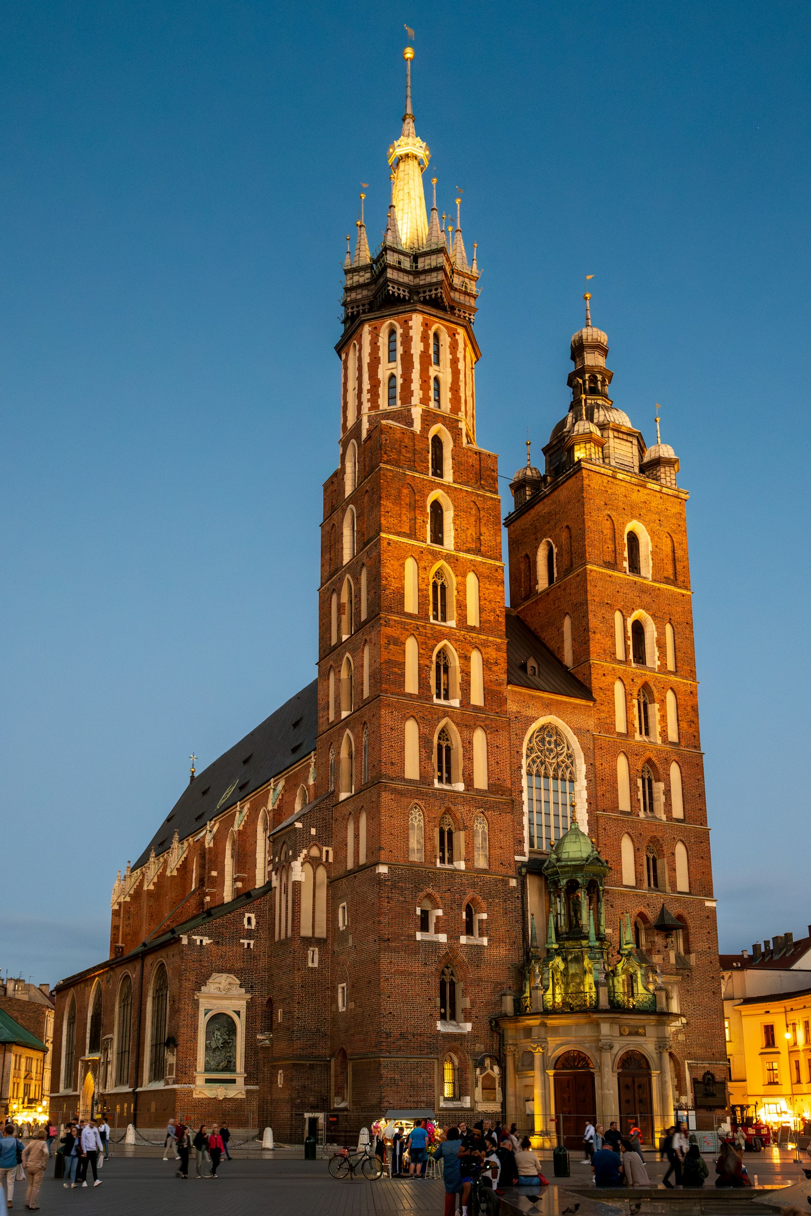 The twin brick-Gothic towers of St Mary's Basilica lit up over Krakow's Main Market Square at dusk