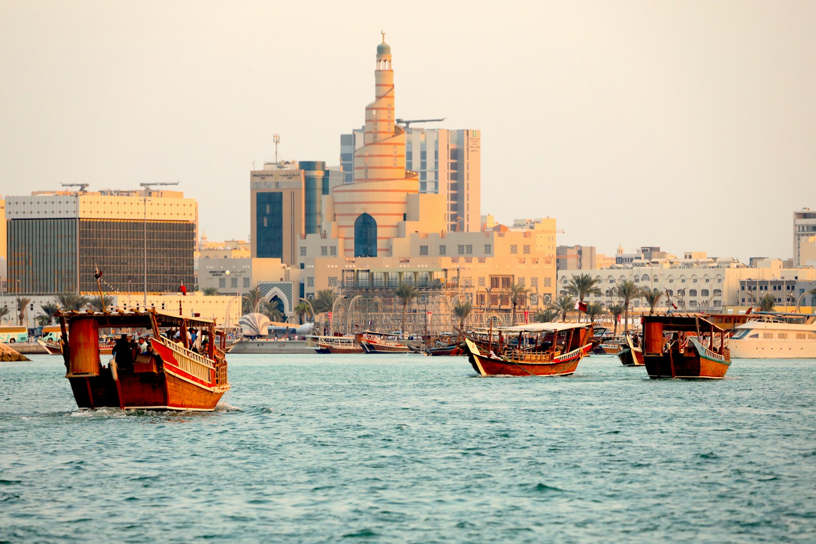 Traditional wooden dhow boats on Doha bay with the spiral Fanar tower behind at golden hour