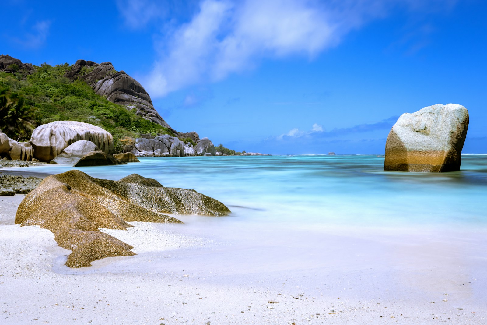 A lone granite boulder standing in milky turquoise water on a white-sand beach, Seychelles