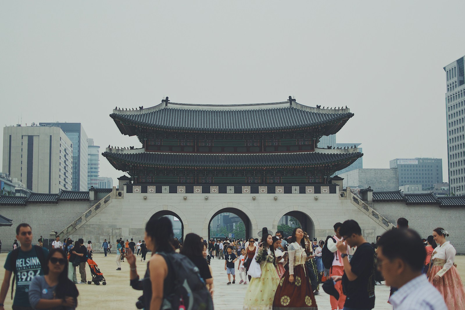 Visitors in hanbok at the Gwanghwamun gate of Gyeongbokgung Palace, with modern Seoul behind