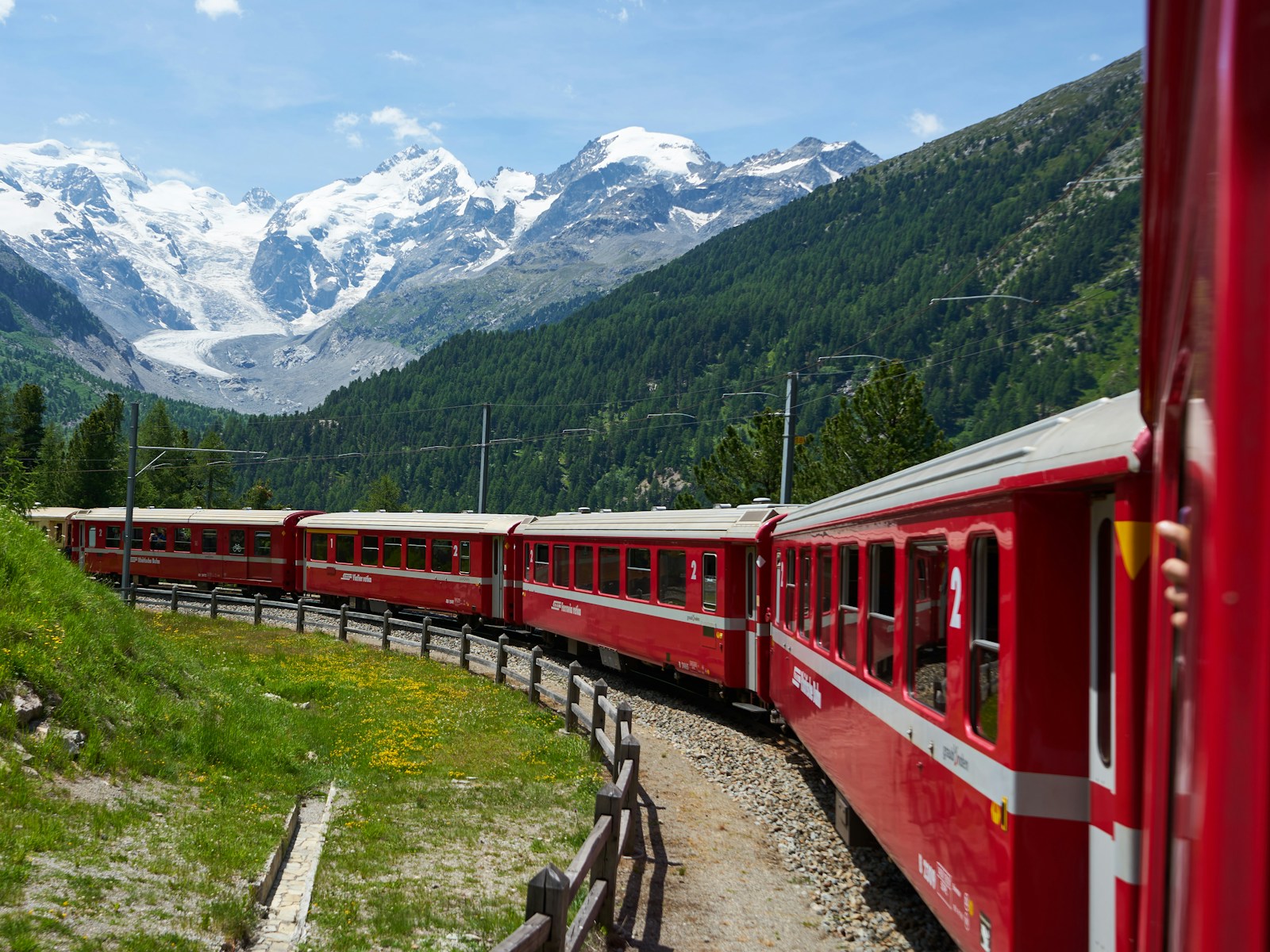 A red Rhaetian Railway train winding below glaciers on the Bernina line