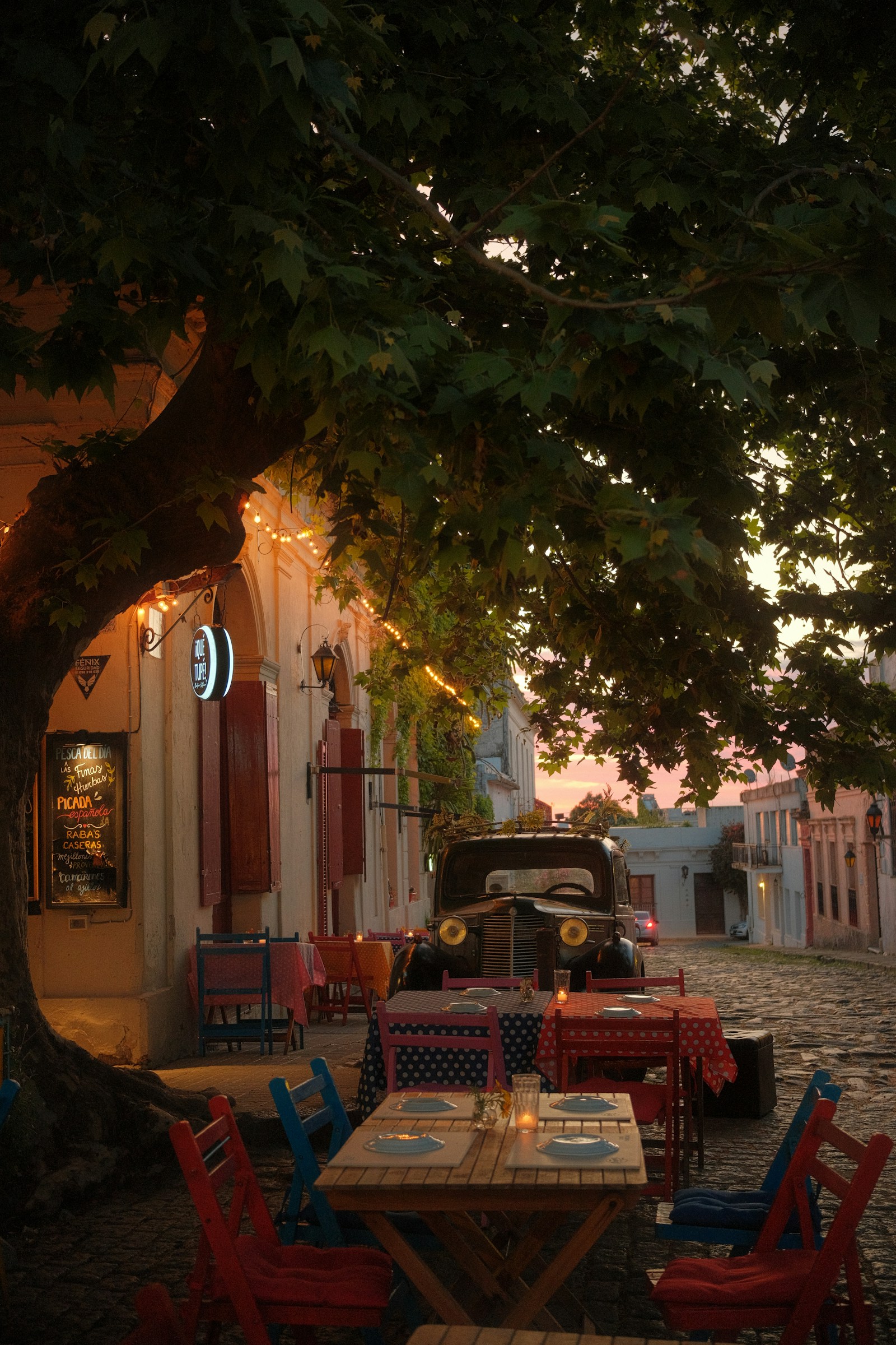 A candlelit cafe and vintage car on a cobblestone street at dusk in Colonia del Sacramento, Uruguay