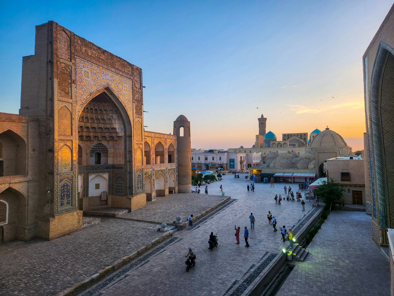A tiled madrasa portal at Poi Kalyan in Bukhara at sunset, with the minaret and dome behind
